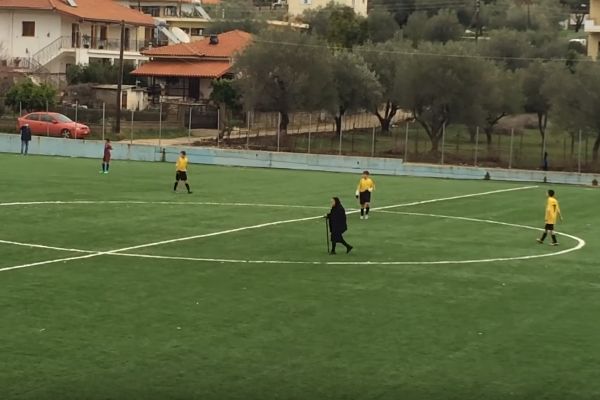 An elderly lady walks across the pitch during a youth match in Greece