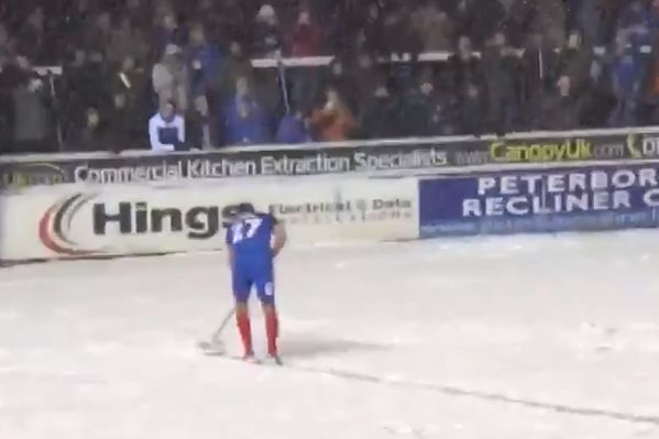 Steven Taylor sweeps snow off the pitch at Peterborough v Walsall