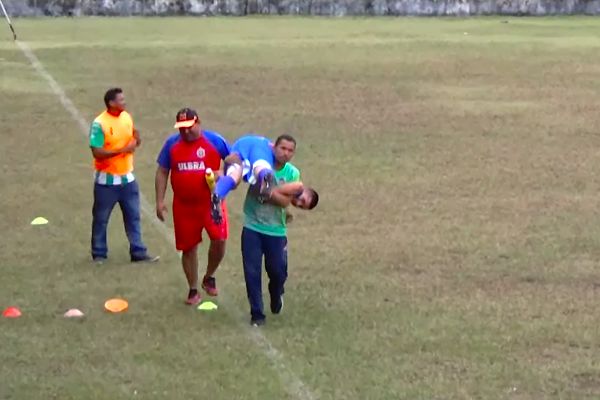 An injured player is carried off the pitch by different people in a Campeonato Amazonense Under-17 match in Brazil