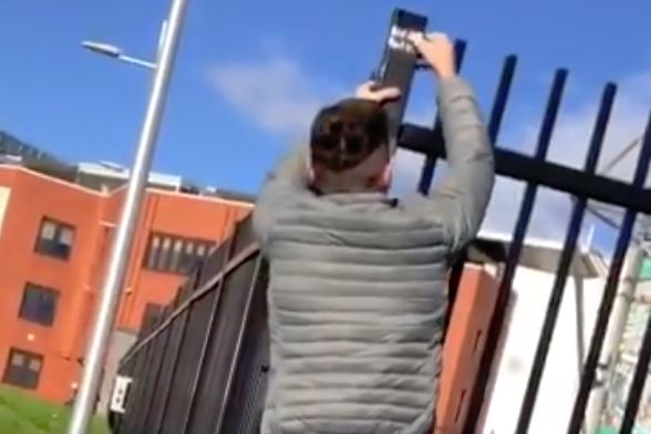A Celtic supporter makes a younger Rangers fan scrape off a sticker he stuck on the railings of Celtic Park