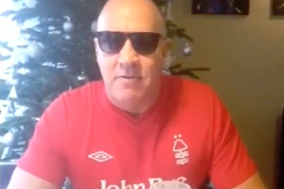 A Nottingham Forest fan sings a Christmas song about Derby County while sitting at a table in a pub with a pint